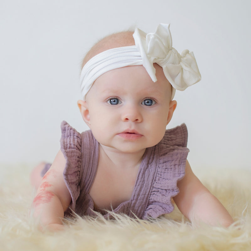Baby wearing a white headband with a large flower on a white background