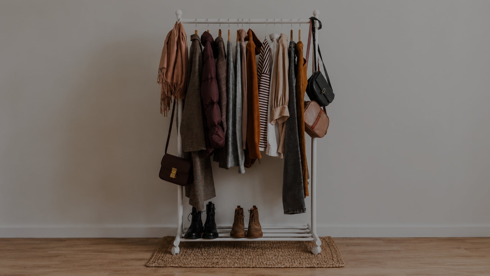 Clothing rack with clothes and bags against a plain wall