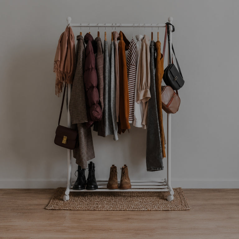 Clothing rack with clothes and bags against a plain wall