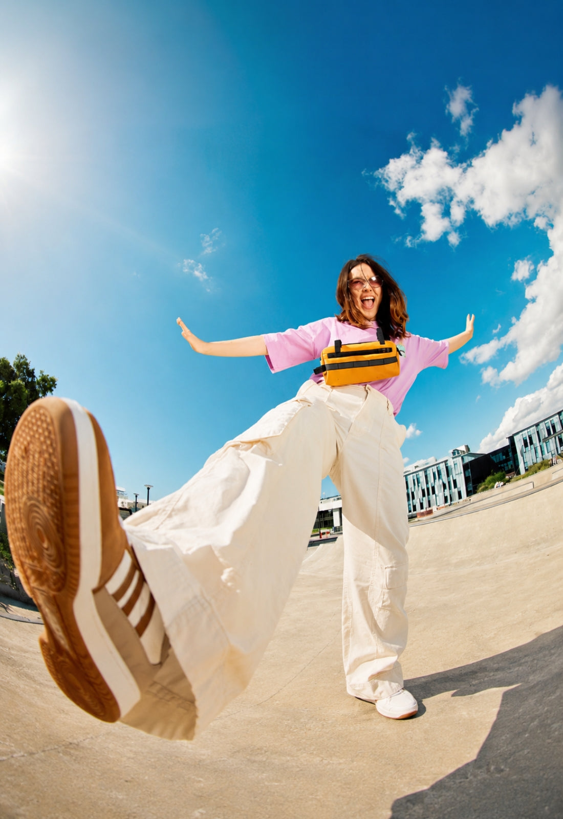 Person in a pink shirt and white pants with a skateboard, jumping in the air on a sunny day.