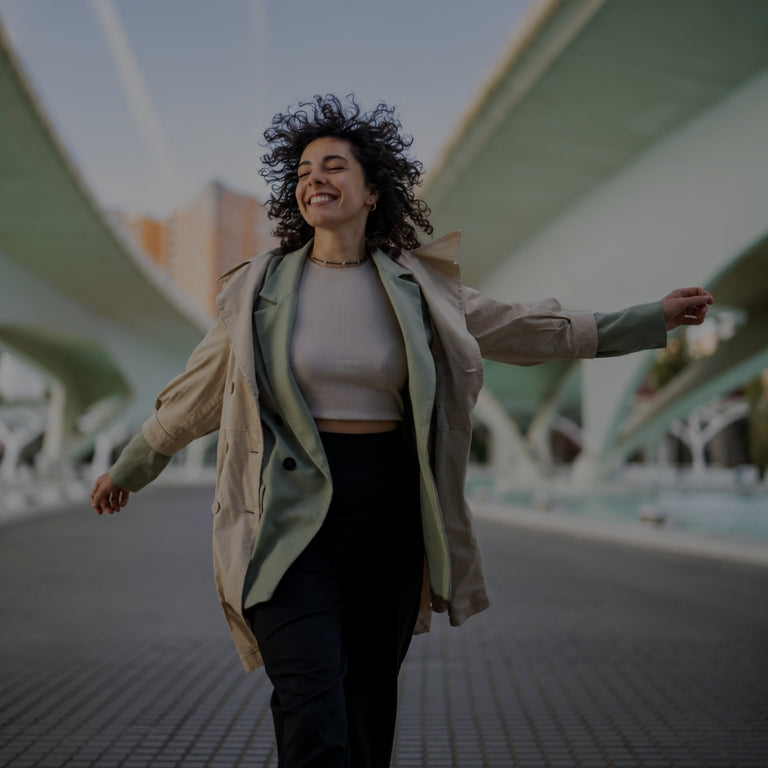 Woman standing with arms outstretched in an urban setting with modern architecture
