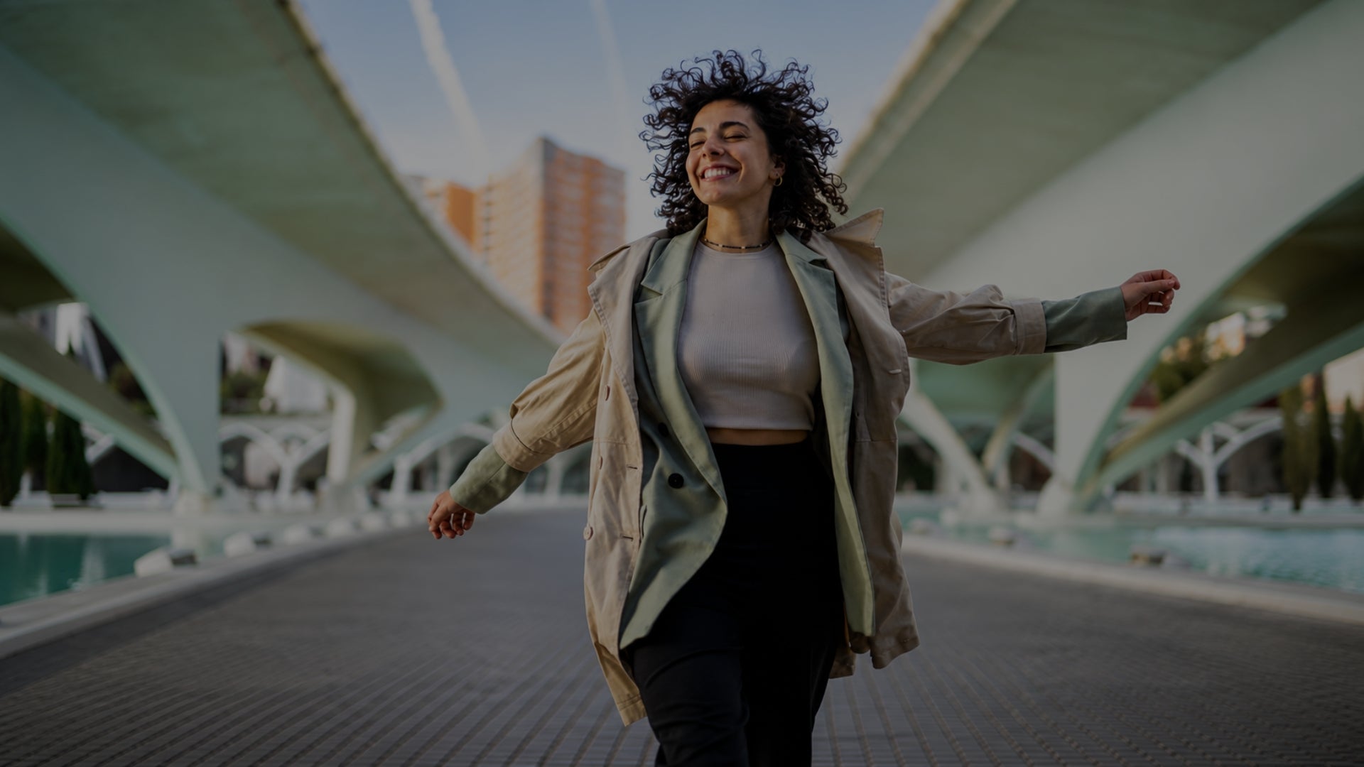 Woman standing with arms outstretched in an urban setting with modern architecture
